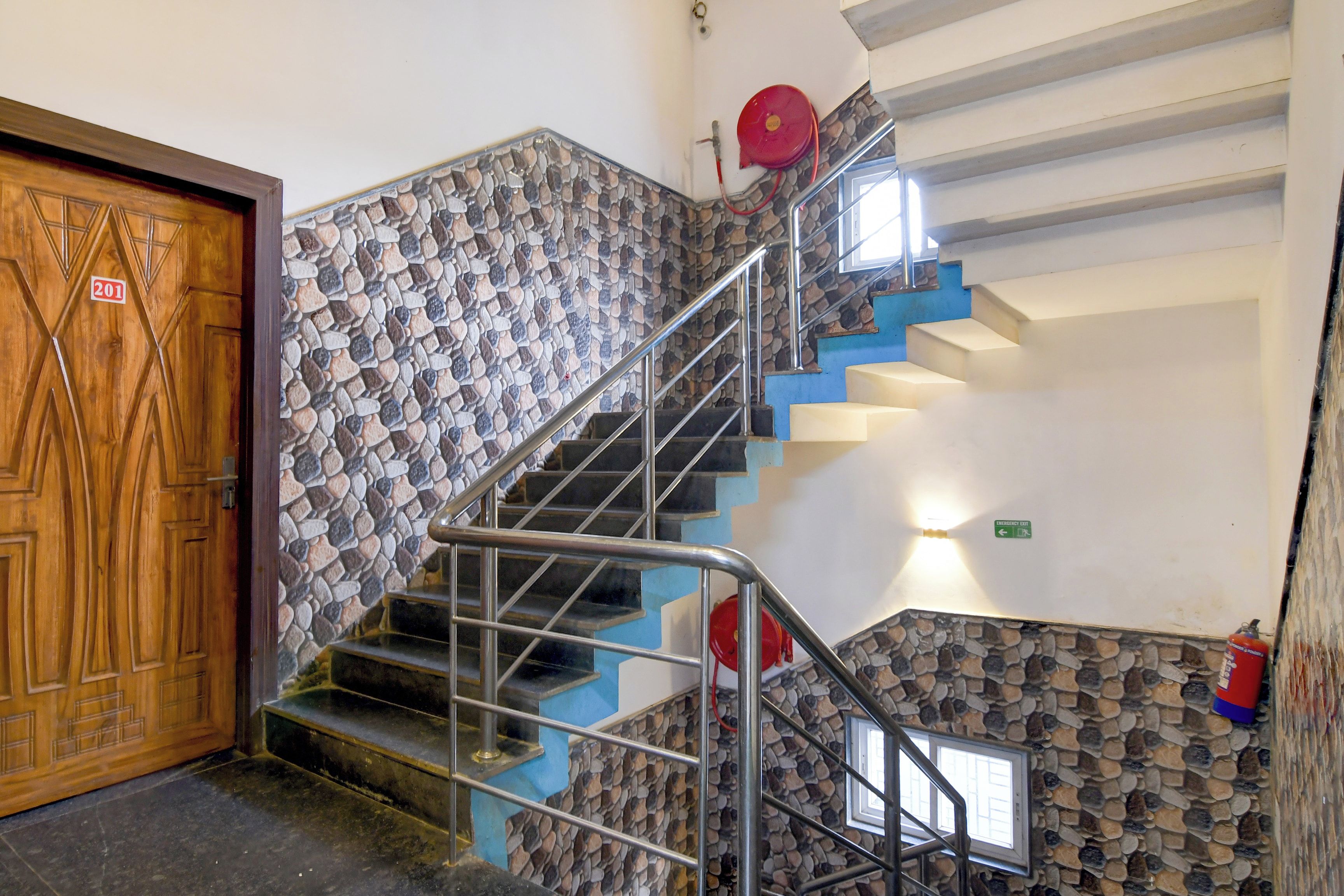 Eine Treppe mit Metallgeländern, eine Holztür mit einer Hausnummer und eine Steinmauer.