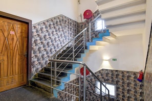 Una escalera con barandas de metal, una puerta de madera con un número y un muro de piedra.
