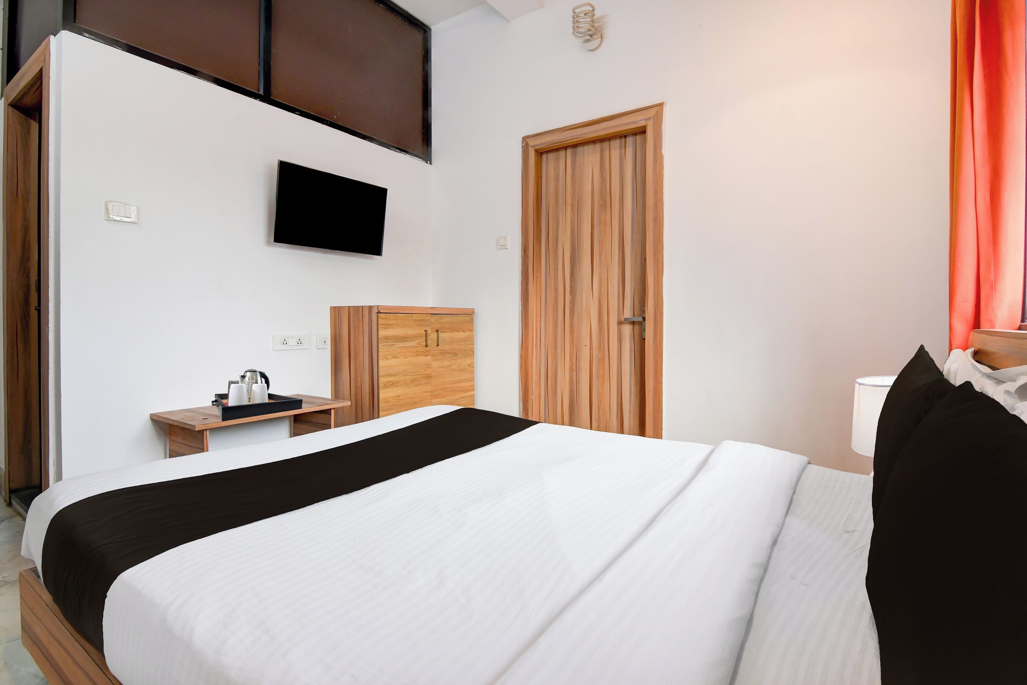 Een hotelkamer met een bed, een aan de muur bevestigde televisie, een houten kast en een klein tafeltje met een waterkoker.