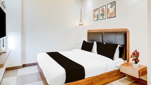 Un dormitorio moderno con estructura de cama de madera, ropa de cama blanca, una mesita de noche con un jarrón de flores y un aplique de pared.