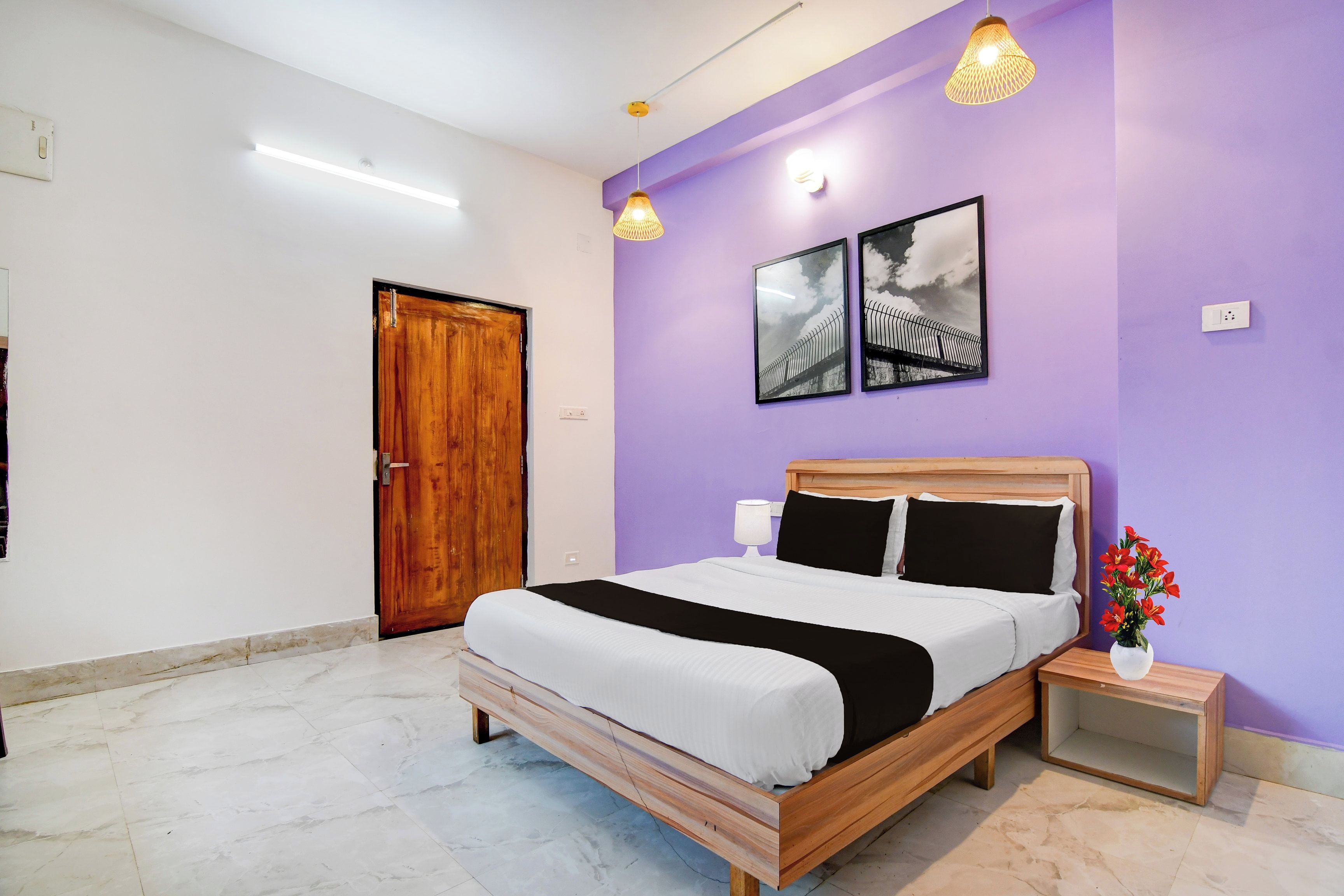 A bedroom with a wooden bed, a nightstand, a wall-mounted lamp, and a framed picture.