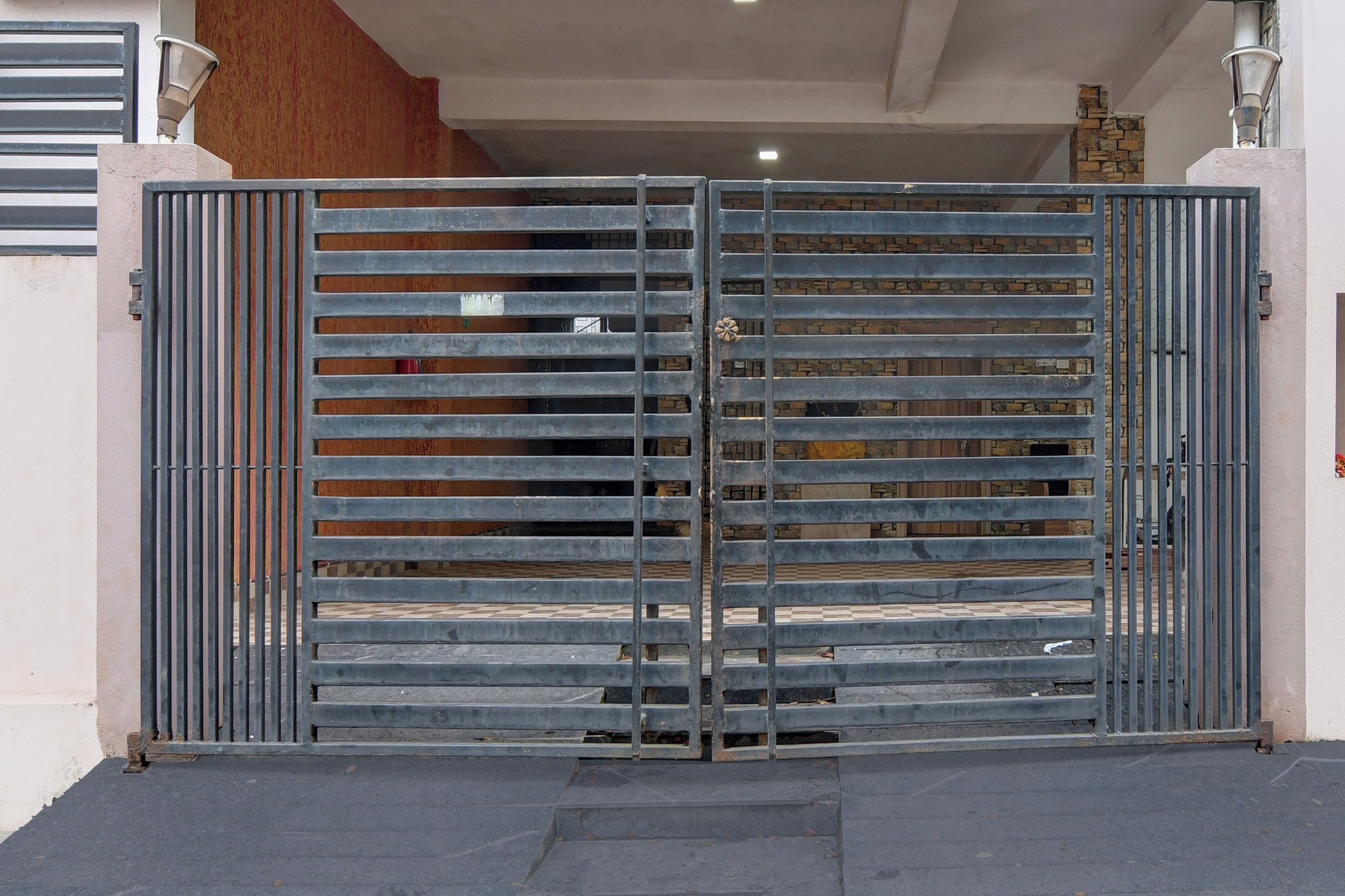 Una reja metálica con barras horizontales, un muro de piedra y un suelo de baldosas.