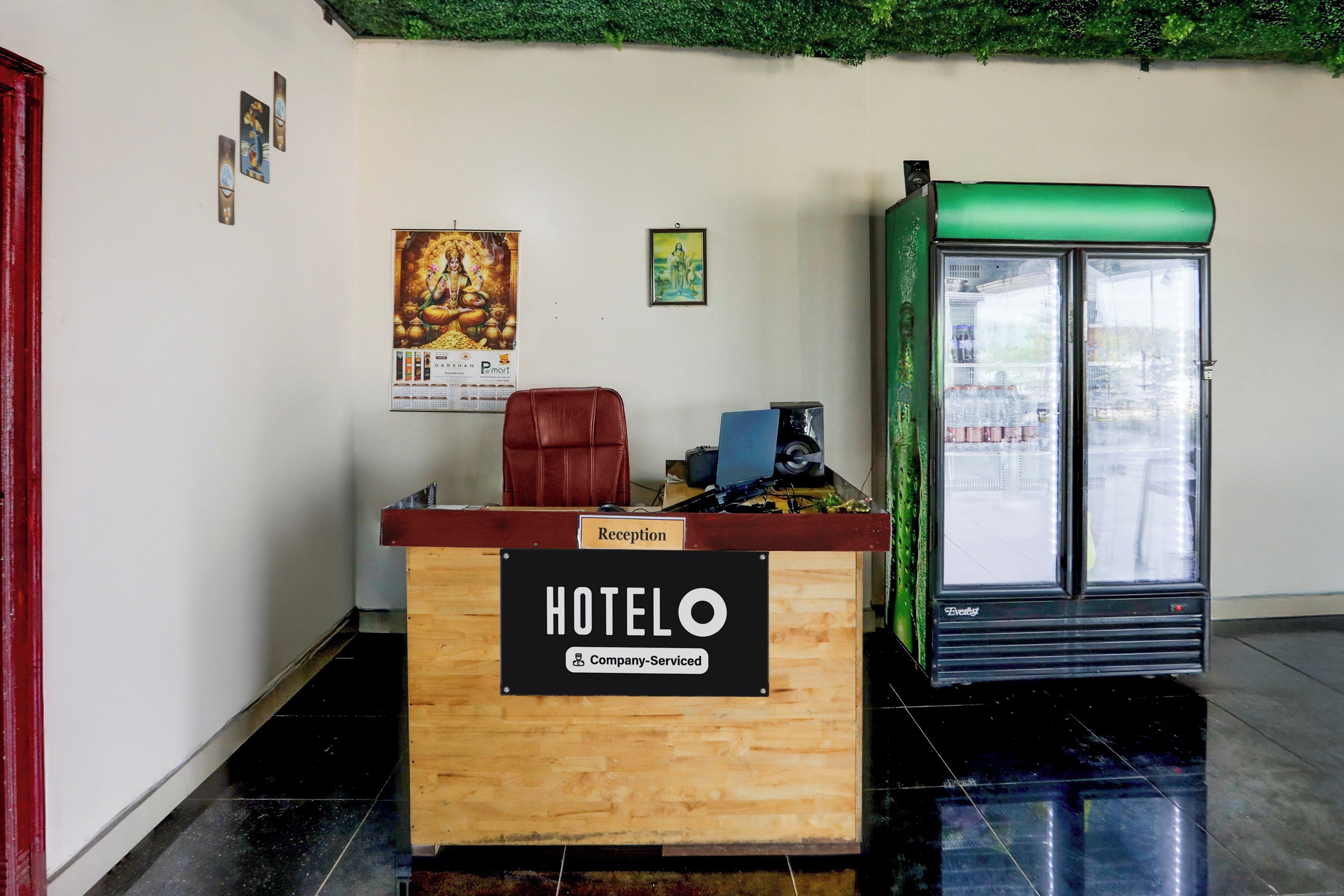 Un mostrador de recepción de hotel con encimera de madera, una silla de cuero rojo y un refrigerador.