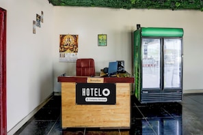 A hotel reception desk with a wooden counter, a red leather chair, and a refrigerator.