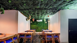 A restaurant interior with a green wall, wooden tables, blue chairs, hanging lights, and a black door. - Hotel O Chirala Beach View (Chirala)