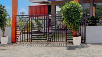 Una entrada protegida por una reja metálica, macetas con plantas y un edificio con techo rojo al fondo.
