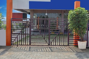 A gated entrance with a metal gate, a potted plant, and a paved pathway leading to a building with a blue and orange facade.