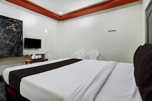 A hotel room with a large bed, a television, a desk with a coffee maker, and a chair.