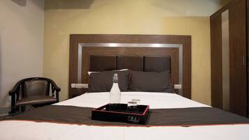 A hotel room with a large bed, a wooden headboard, a bedside table with a bottle and glasses, and a chair.