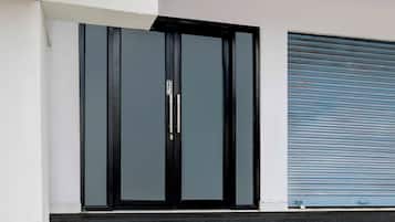 A modern building facade with a black-framed glass door and a blue roller shutter.