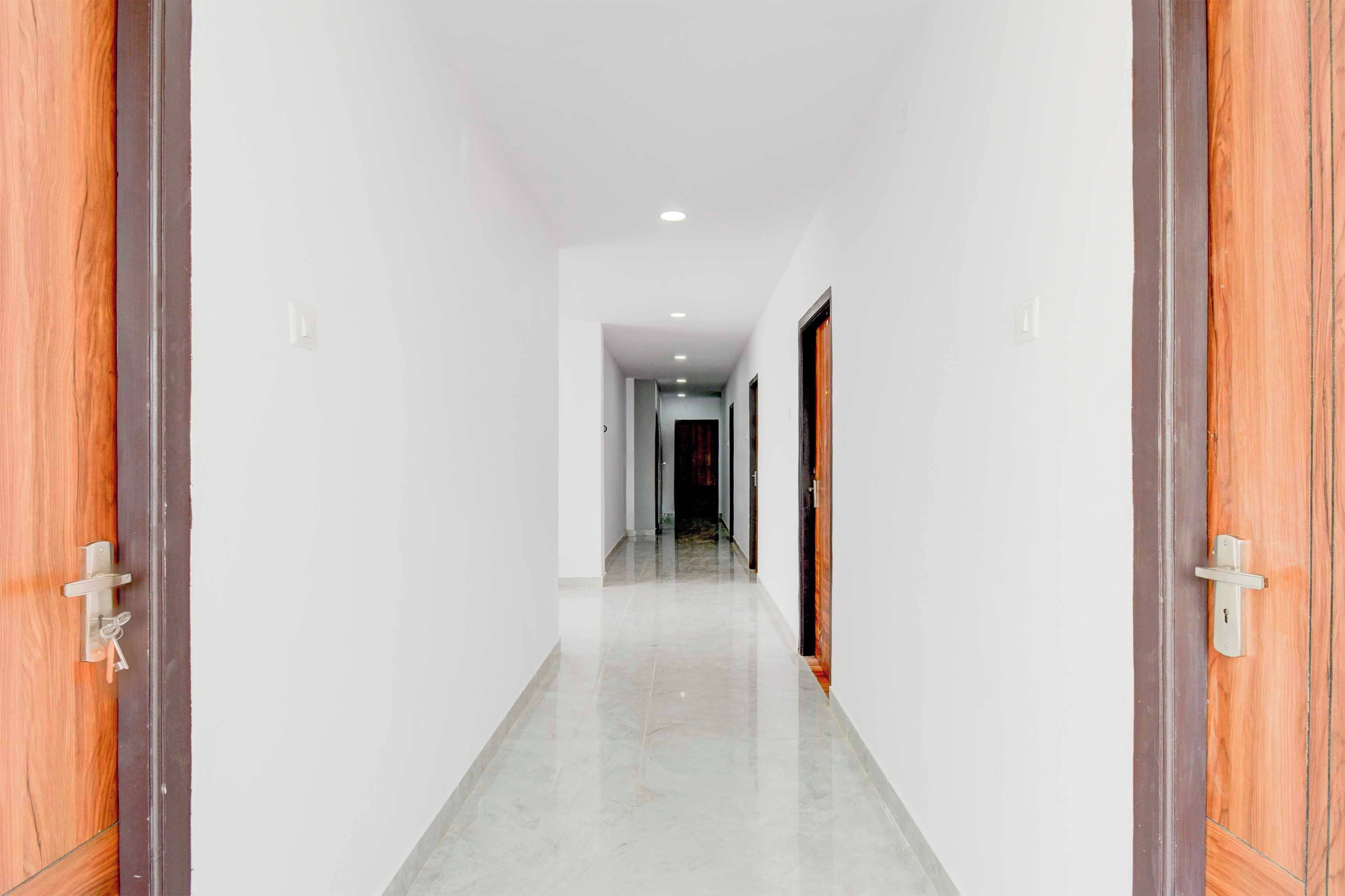A corridor with white walls and a tiled floor, leading to a door with a wooden frame.