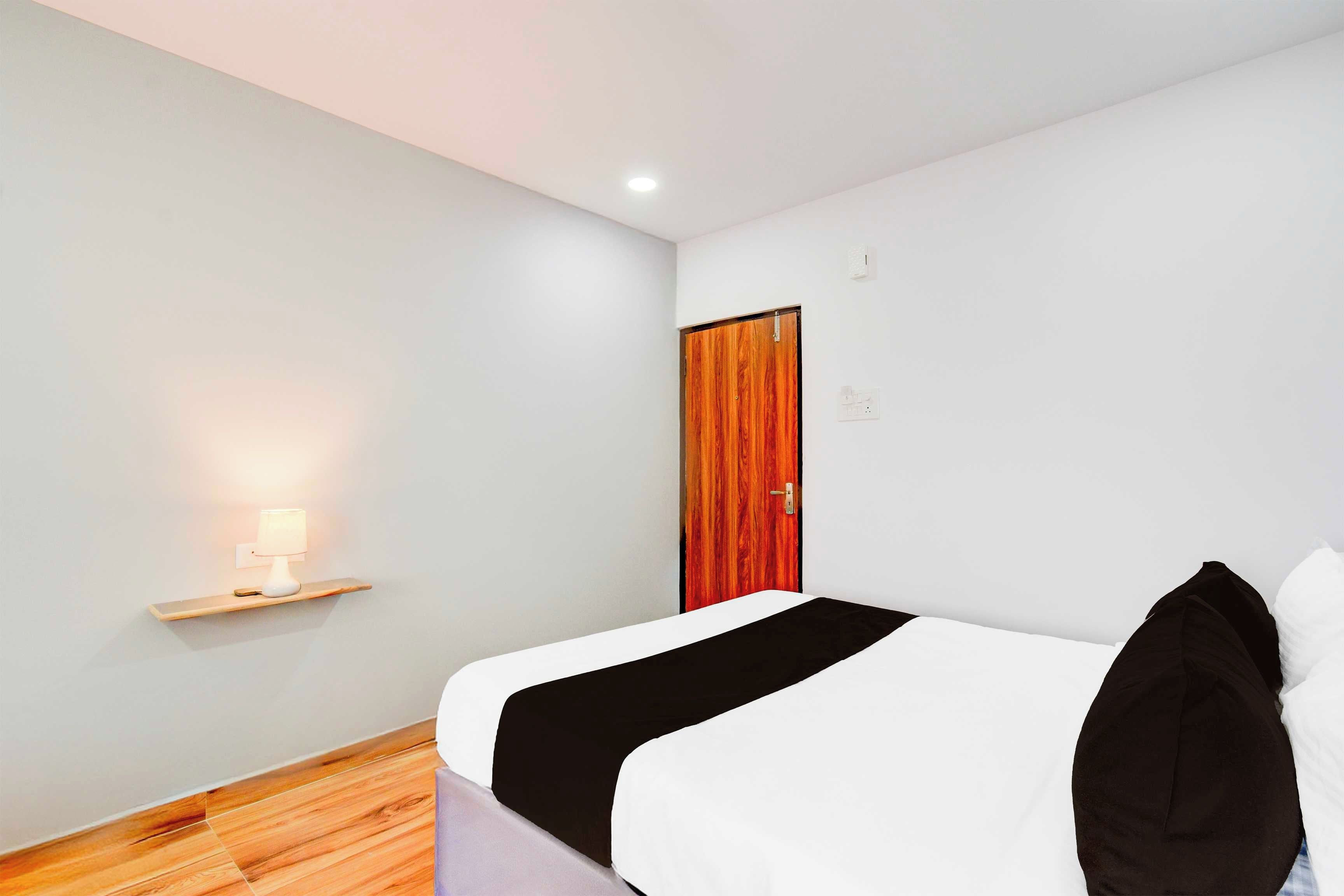 Habitación de hotel con una cama, una mesita de noche con lámpara, una puerta de madera y un interruptor de luz en la pared.