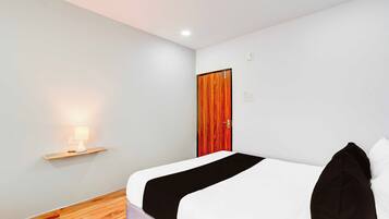 Habitación de hotel con una cama, una mesita de noche con lámpara, una puerta de madera y un interruptor de luz en la pared.