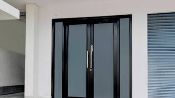 Puerta doble negra con manija, incrustada en una pared blanca con un persiano azul a la derecha.