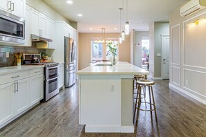 A modern kitchen with white cabinetry, stainless steel appliances, and a central island with stools. - All-Seasons Everett Escape w/ Private Balcony! (Everett)