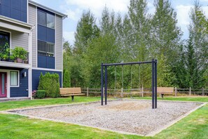 A playground with a swing set and benches, surrounded by a building with a balcony and potted plants. - All-Seasons Everett Escape w/ Private Balcony! (Everett)