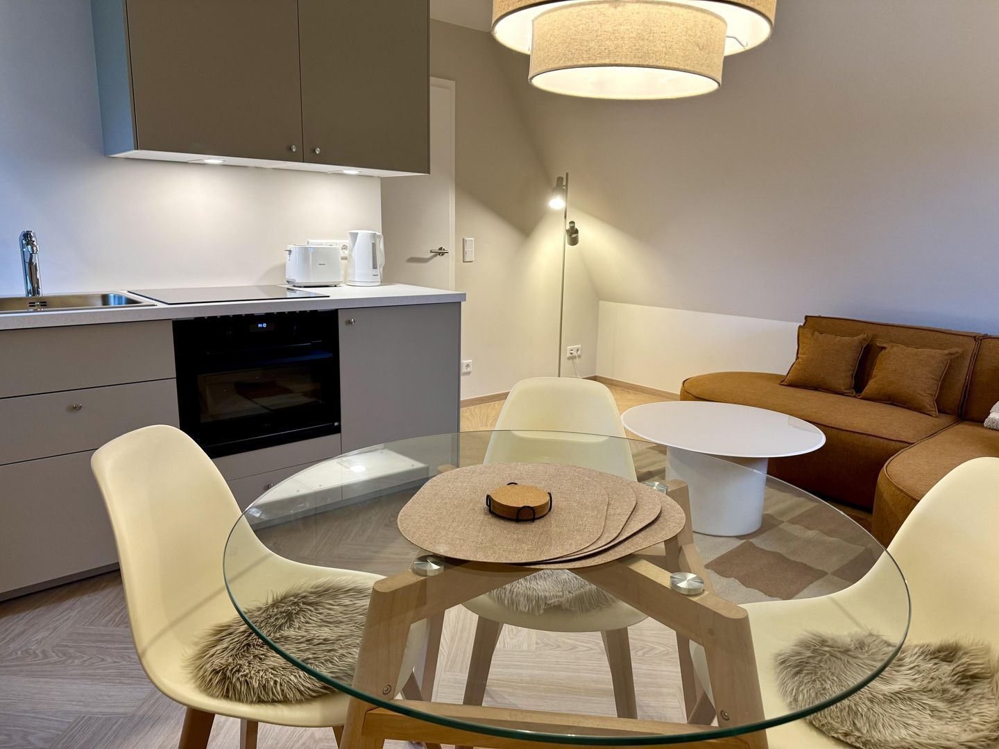 Eine moderne Küche mit Einbauofen, ein Essbereich mit Glastisch und ein braunes Sofa.