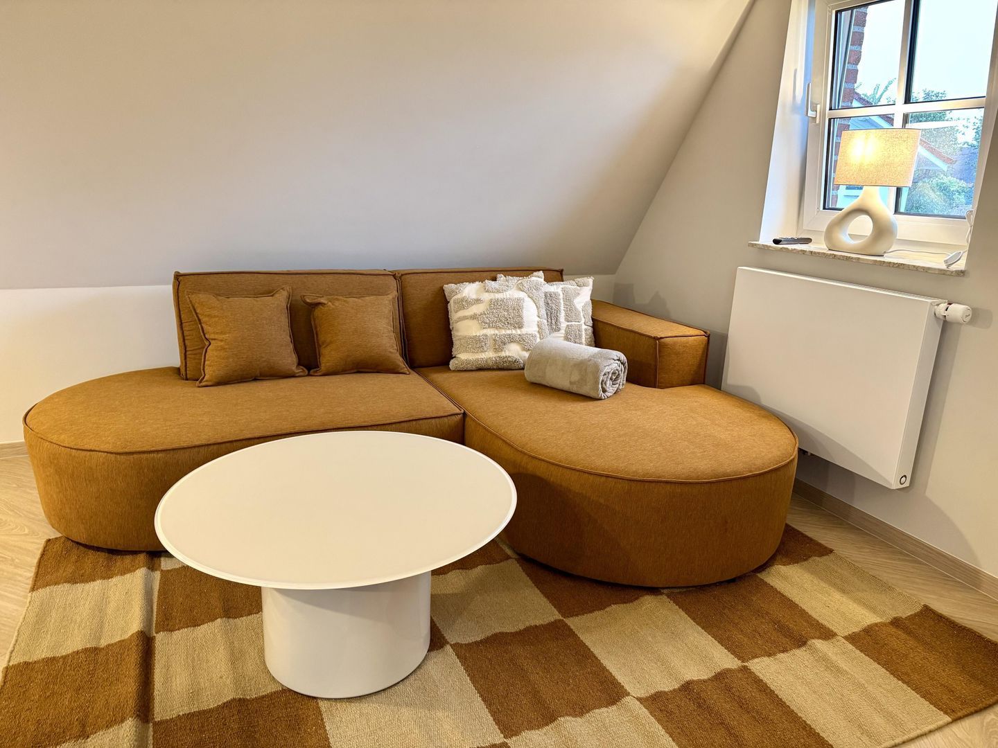 Ein modernes Wohnzimmer mit einem Ecksofa, einem runden Couchtisch und einem Schachbrettmuster-Teppich.