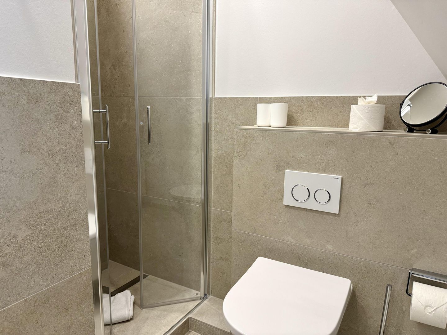 Ein modernes Badezimmer mit Duschkabine aus Glas, einer weißen Toilette und einem Handtuchhalter.