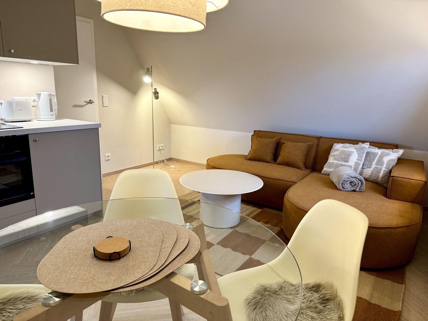 En moderne stue med en sofa, to stole, et sofabord og et køkkenområde med en mikrobølgeovn.