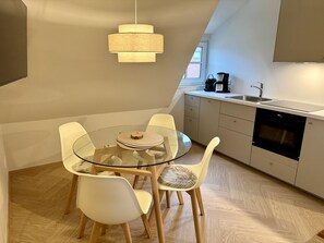 Eine moderne Küche mit einem runden Glastisch, weißen Stühlen, einer Hängeleuchte und einem eingebauten Backofen.