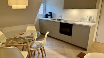 Et moderne køkken med et glasbord, hvide stole, indbygget ovn og kaffemaskine.