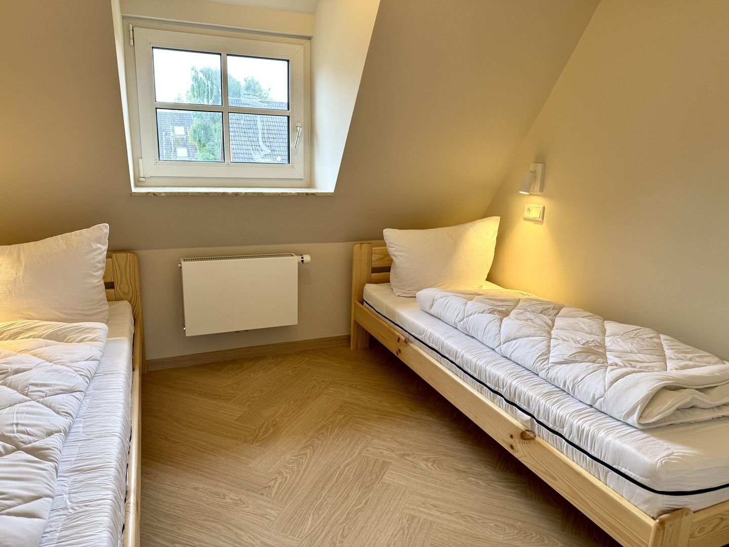 Ein Zimmer mit zwei Etagenbetten, einem Fenster, einem Heizkörper und einer Wandleuchte.