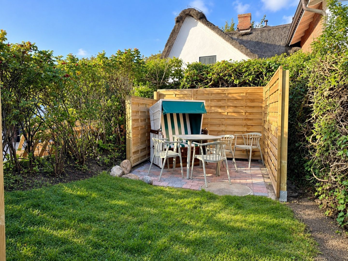 Eine Terrasse mit Tisch und Stühlen, umgeben von einem Holzzaun und Grünpflanzen.