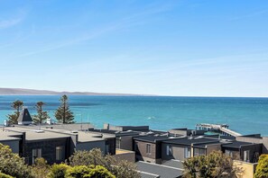 A coastal residential area with modern buildings, a pier extending into the sea, and clear skies. - Oceanscapes - U15 Point Grey Lorne (Lorne)