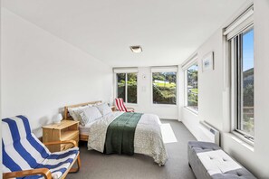 Un dormitorio con cama, una silla, una mesita de noche y una ventana.