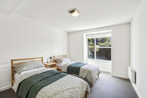 A bedroom with two single beds, a window with a view of greenery, and a ceiling light fixture. - Oceanscapes - U15 Point Grey Lorne (Lorne)