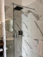 A modern bathroom with a glass-enclosed shower, a marble-tiled wall, a sink, and a mirror.