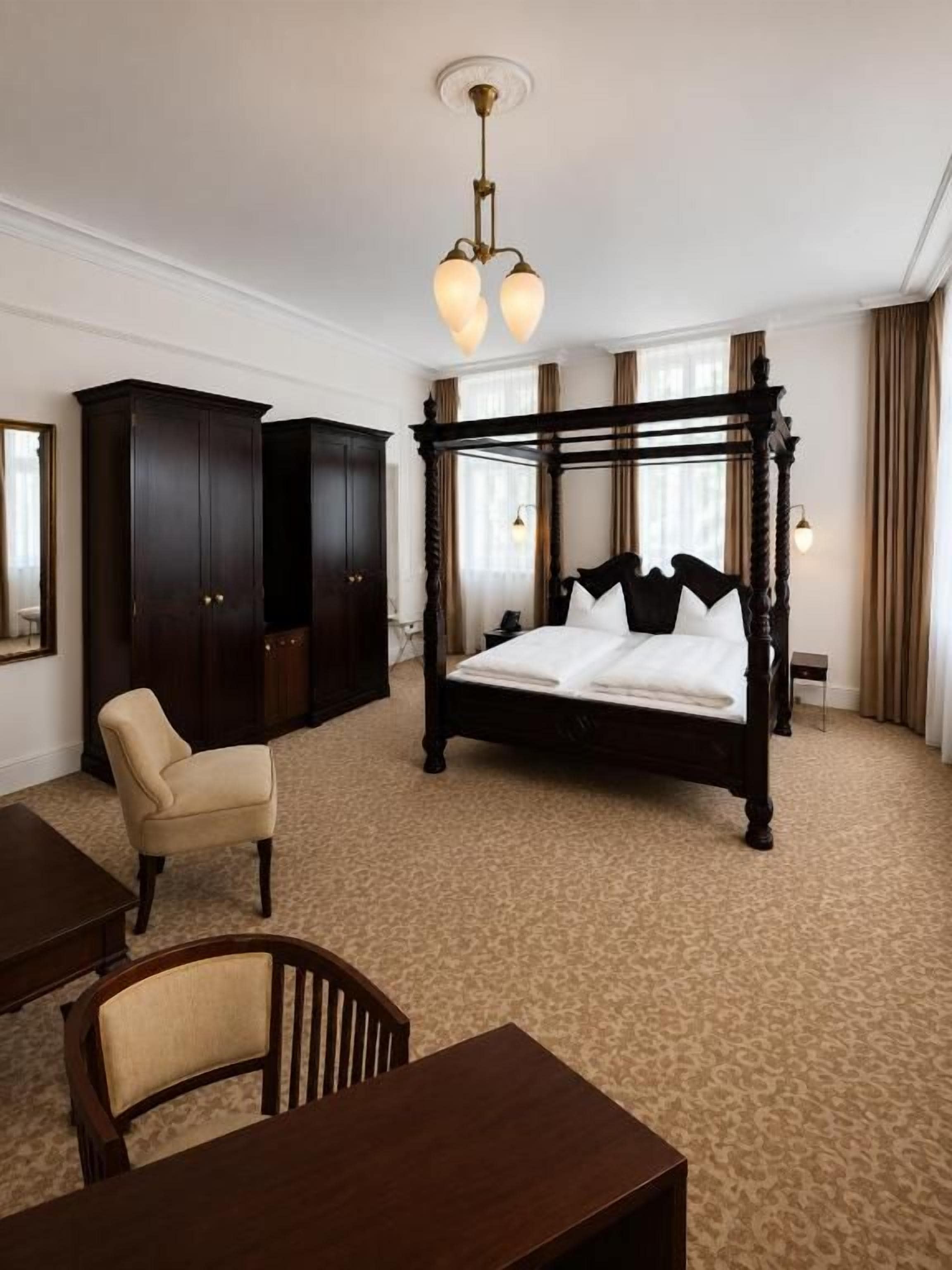 Habitación de hotel con cama con dosel, armario de madera, escritorio con silla y suelo alfombrado.