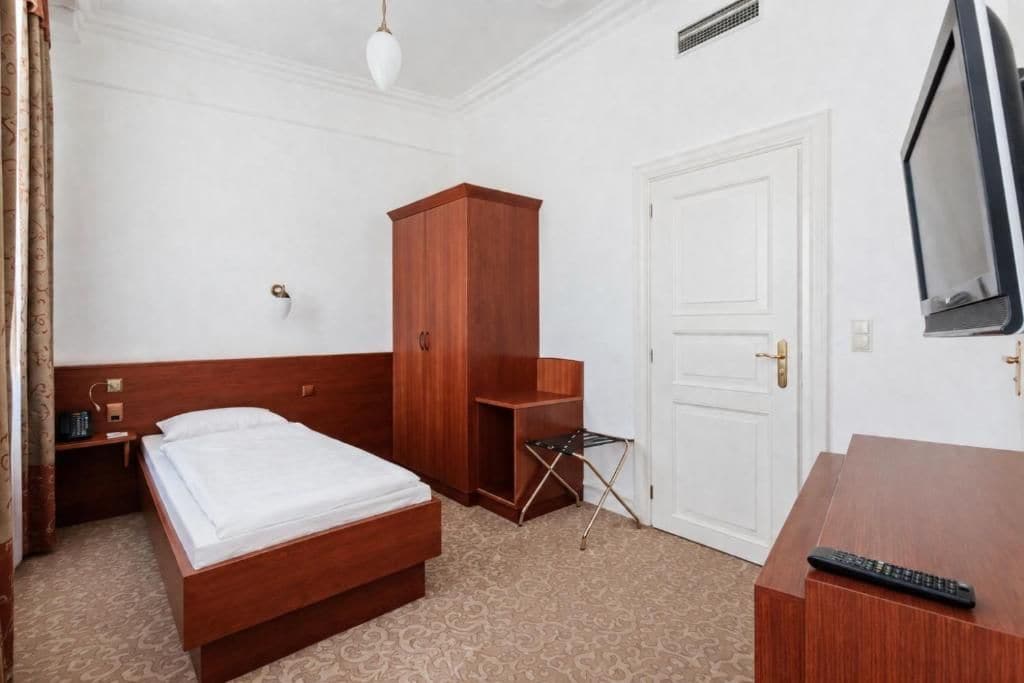A hotel room with a wooden bed, a wardrobe, a desk with a television, and a door.