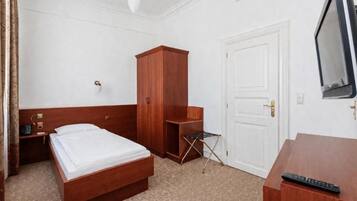A hotel room with a wooden bed, a wardrobe, a desk with a television, and a door.