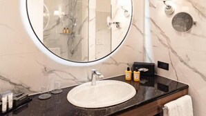 A bathroom with a round mirror, a sink, and marble walls. - Hotel Fürstenhof (Bad Pyrmont)