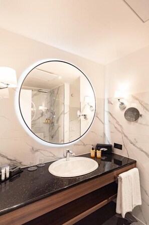 A bathroom with a round mirror, a sink, and marble walls. - Hotel Fürstenhof (Bad Pyrmont)