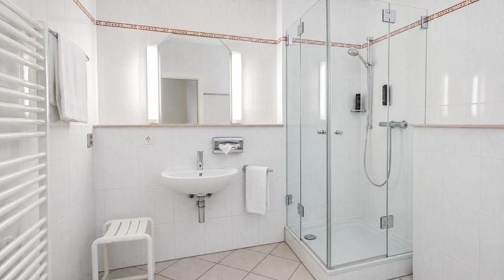 A modern bathroom with a glass shower enclosure, a white sink, and a small white stool.