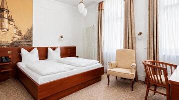 A hotel room with a double bed, a chair, a desk, and a large window with curtains.