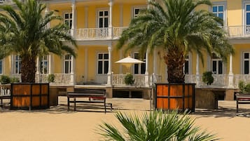 A multi-story hotel with balconies, palm trees, and a sandy courtyard.