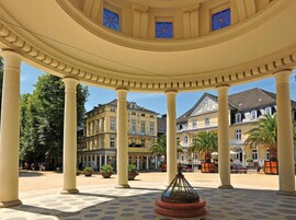 Un patio cubierto con columnas, una fuente central y edificios al fondo.