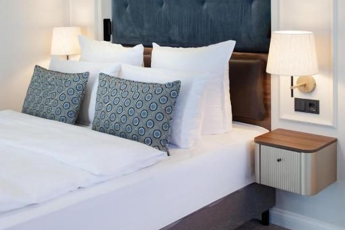 A hotel room with a large bed, two bedside tables, and a wall-mounted light fixture.