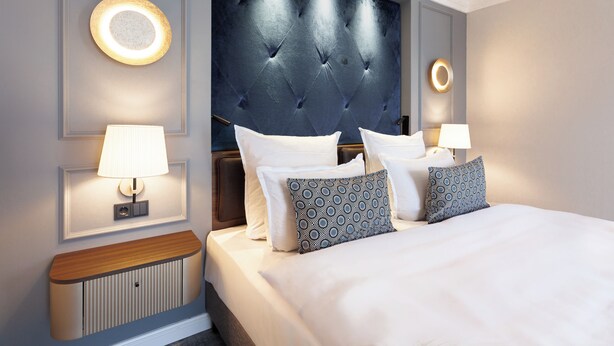 A hotel room with a large bed, two bedside lamps, a wall-mounted light, and a decorative headboard.