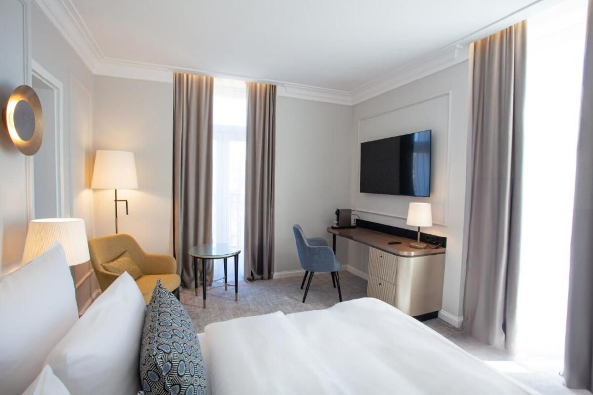 A hotel room with a bed, a desk, a TV, a chair, and a lamp.
