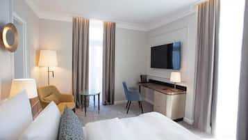 A hotel room with a bed, a desk, a TV, a chair, and a lamp.