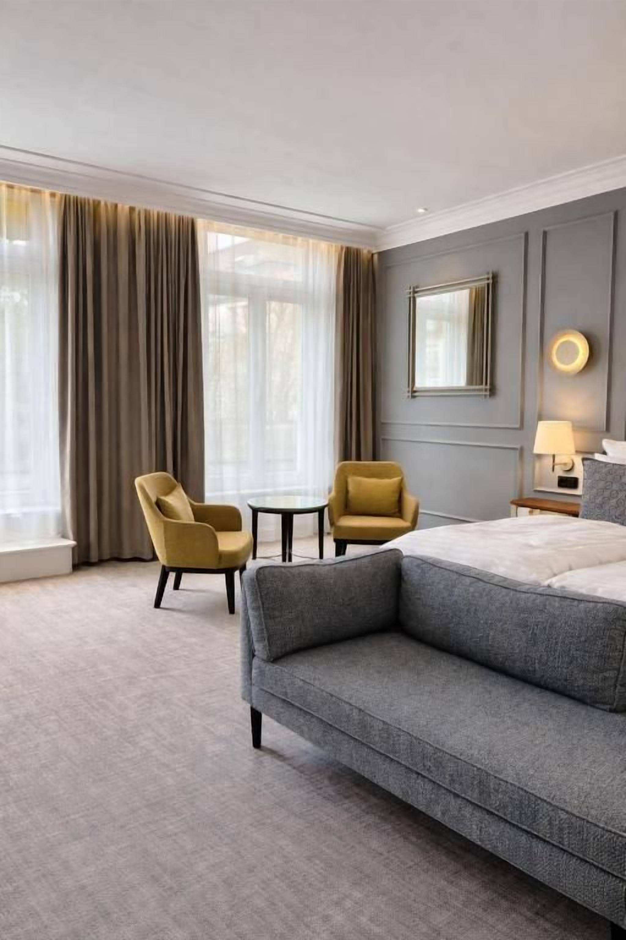 Een hotelkamer met een groot bed, twee fauteuils, een tafeltje en een raam met gordijnen.