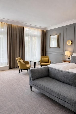 Una habitación de hotel con una cama grande, dos sillones, una mesita y una ventana con cortinas.