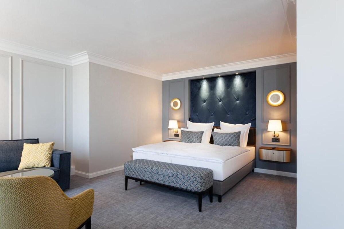 A hotel room with a bed, bedside tables, a sofa, and a chair.