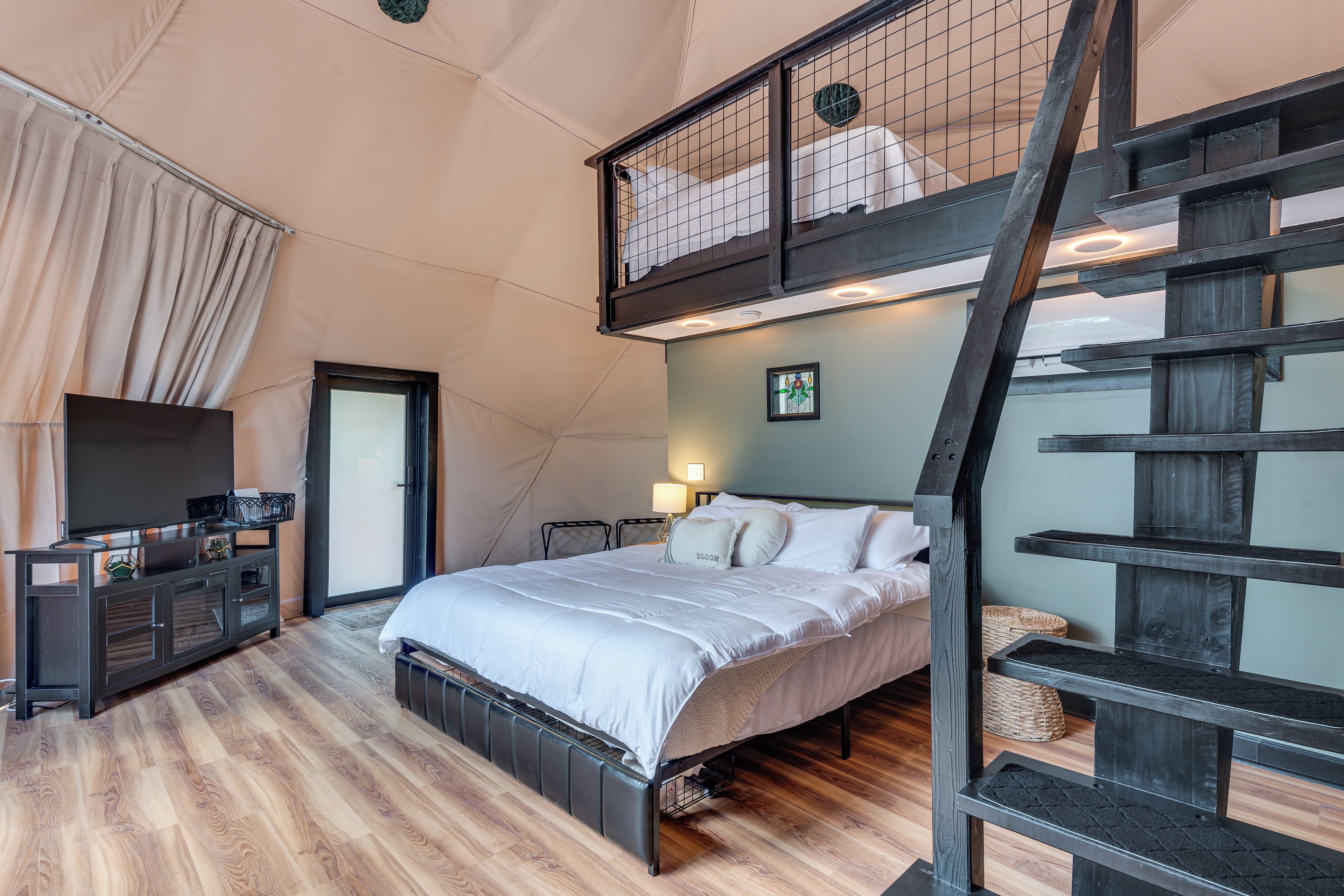 A bedroom with a bed, a TV, a desk, and a staircase.