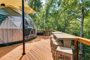 Eine Holzterrasse mit überdachter Sitzgelegenheit und einer gläsernen Kuppelstruktur.